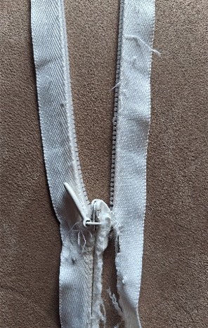 Damaged No. 3 nylon coil zip cut out of a wedding dress, showing frayed tape, distorted teeth and a strained slider