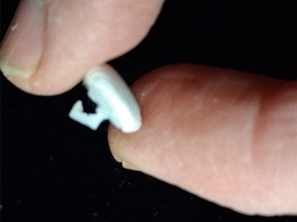 Front face of a satin covered wedding dress button held between two fingers
